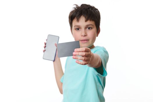 Focus on black credit card with free space for advertising text, in the hands of blurred school boy holding smartphone with blank screen, isolated on white backgroun. Internet banking. Online shopping