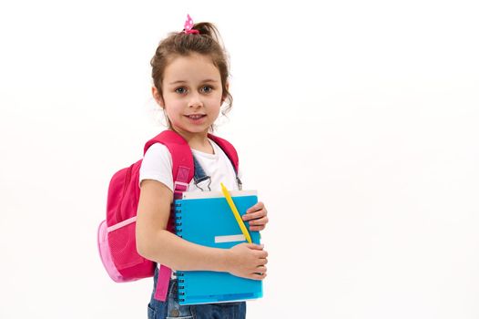 Adorable child girl, primary school student, first grader with copybook and pink backpack, isolated on white background