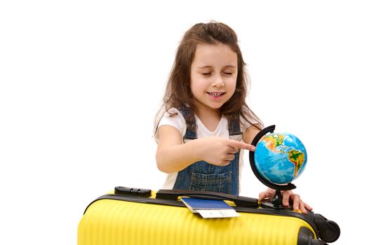 Little child girl points to travel destination on the Earth world globe, chooses a country to visit at summer holidays