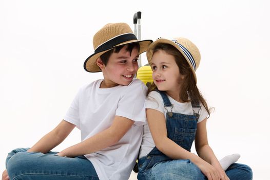 Two diverse kids travelers in casual wear, with suitcase smile look at each other, on white background. Free ad space