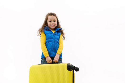 Isolated portrait on white background of a happy baby girl smiling a cheerful toothy smile, carrying a yellow suitcase