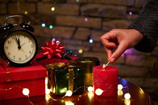 Black alarm clock with midnight on dial and woman's hand lights candle with matches. Merry Christmas