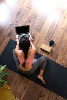 Vertical image of top view of young woman using laptop to search online yoga class. Copy space.