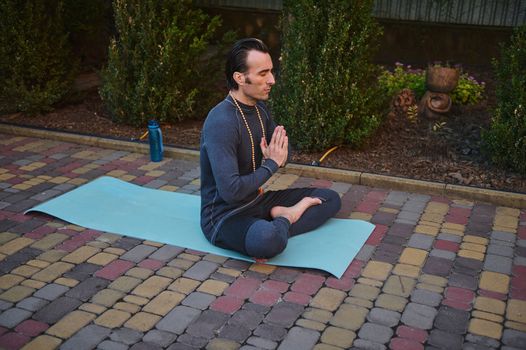 Male yogi keeping hands palms together, meditates on a fitness mat with rosary beads. Yoga practice. Mindfulness