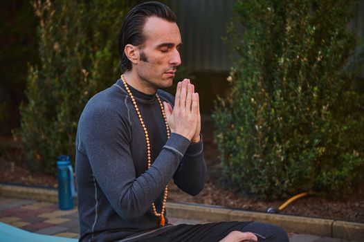 Close-up portrait of peaceful man yogi practicing yoga outdoors, meditating putting palms together. Prayer and gratitude