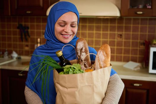 Healthy purchasing from grocery. Charming Middle-Eastern Muslim woman in hijab, unpacks a shopping bag with healthy food