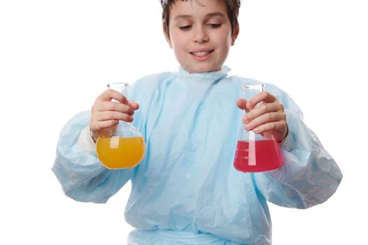 Selective focus on laboratory glassware with colored chemicals in the hands of school kid in lab coat doing experiments