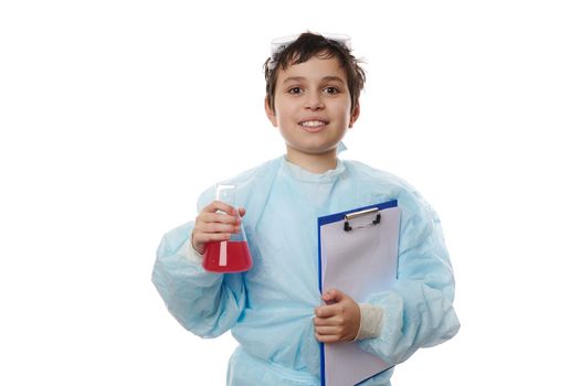 Teenage schoolboy, young chemist scientist in lab coat, holds clipboard and flat-bottomed flask with red chemical liquid