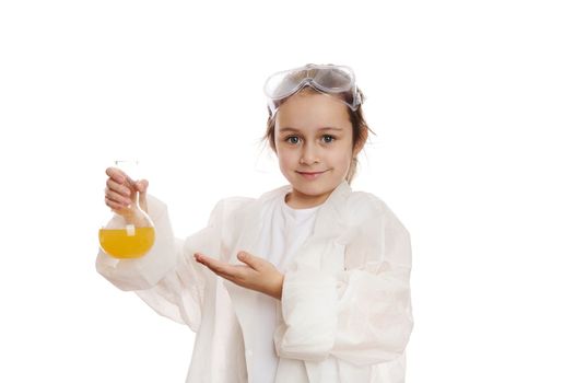 Smart schoolgirl, young chemist at chemistry class, points at laboratory flask with liquid chemical, looking at camera