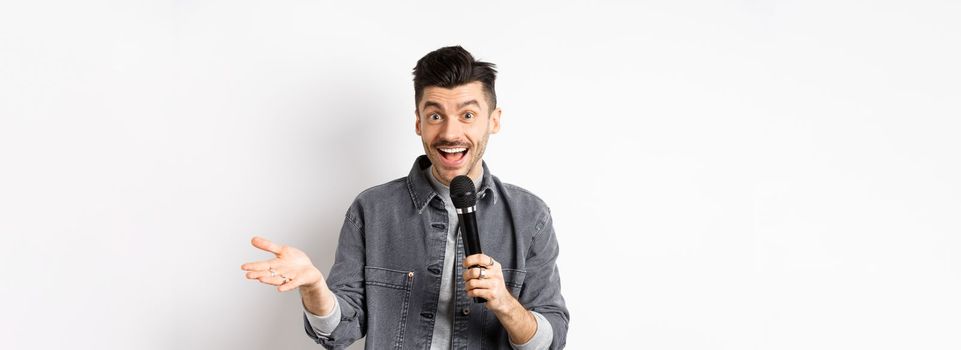 Handsome smiling performer talking in mic, gesturing and performing, making speech with microphone, standing against white background