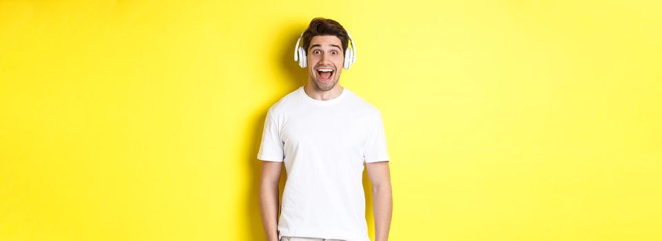 Man in headphones looking surprised, standing against yellow background in white outfit
