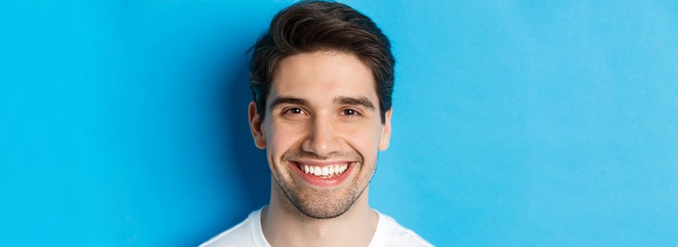 Head shot of handsome young man with beard, smiling happy over blue background. Copy space