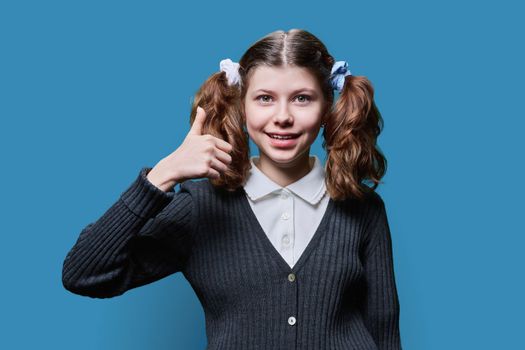 Preteen schoolgirl showing thumbs up ok sign, on blue background