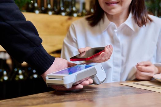 Woman in restaurant paying for an order using smartphone and terminal