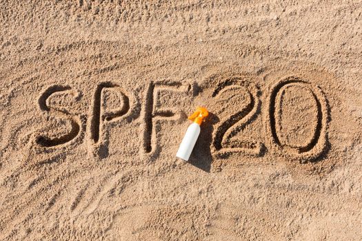 Sun protect factor twenty. SPF 20 word written on the sand and white bottle with suntan cream. Skin care concept background.