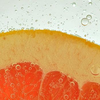 Close-up of fresh grapefruit slice on white background. Slice of red grapefruit in sparkling water on white background, close-up. Horizontal image