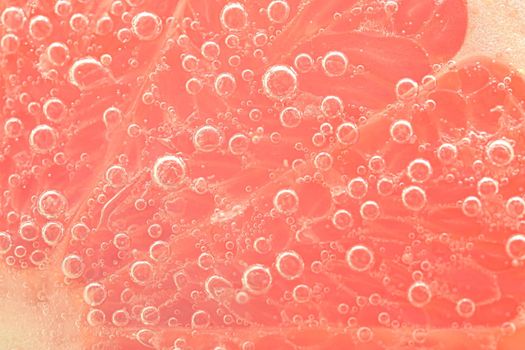 Close-up of a grapefruit slClose-up of fresh orange slice on white background. Slice of orange in sparkling water on white background, close-up. Horizontal image.ice in liquid with bubbles. Slice of red ripe grapefruit in water. Close-up of fresh grapefruit slice covered by bubbles.