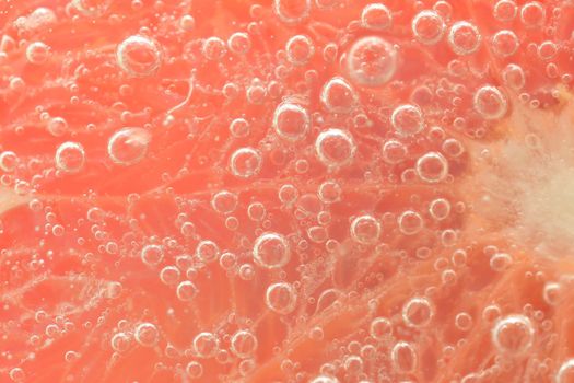 Close-up of a grapefruit slice in liquid with bubbles. Slice of red ripe grapefruit in water. Close-up of fresh grapefruit slice covered by bubbles