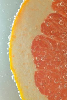 Close-up of fresh grapefruit slice on white background. Slice of red grapefruit in sparkling water on white background, close-up. Vertical image