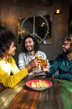 Vertical portrait of happy male friends in a bar enjoying drinks together toasting with beer, having fun. Lifestyle concept.