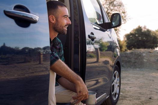 smiling man in the door of a camper van with a mug