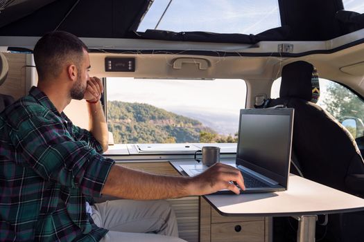 man working on his laptop from his camper van