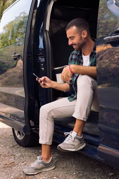 man using his phone sitting in the door of his van