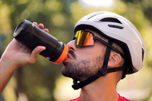 man with helmet and cycling goggles drinking water