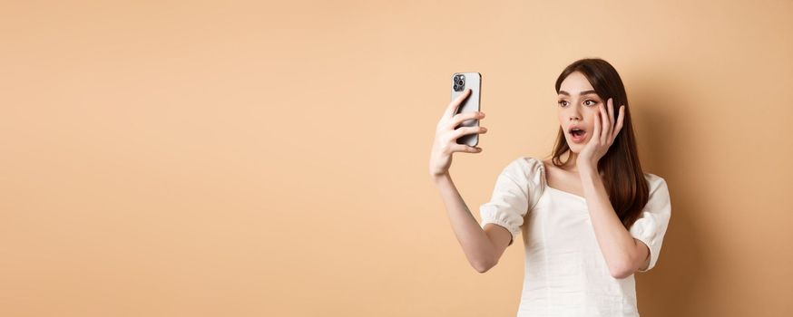 Fashion girl record smartphone blog, taking selfie on cellphone, standing on beige background