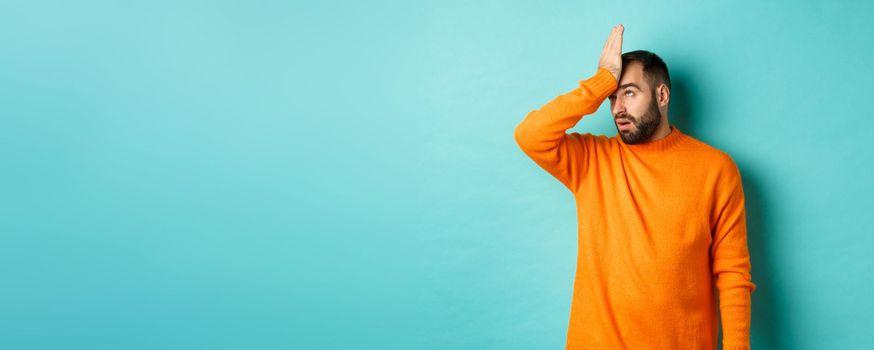 Annoyed man roll eyes and making facepalm, standing over turquoise background