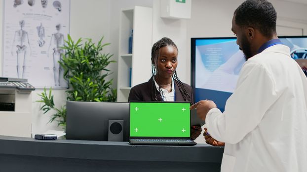 Medical specialists working at reception with greenscreen on laptop