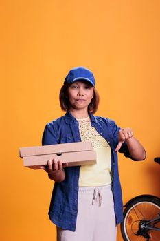 Serious pizzeria delivery worker doing disapproval sign while holding carton cardboard