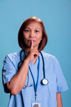 Old physician nurse showing shhh taboo sign with finger to lips while working at health care expertise