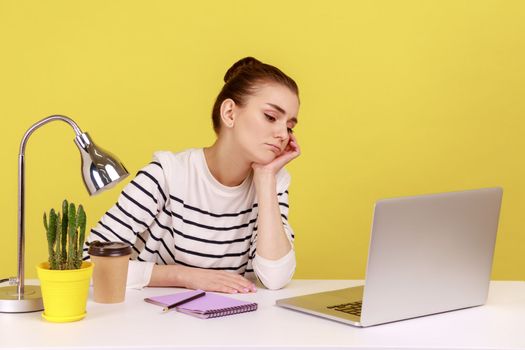 Woman looking at laptop screen, leaning on hand, feeling lazy uninterested in her job.