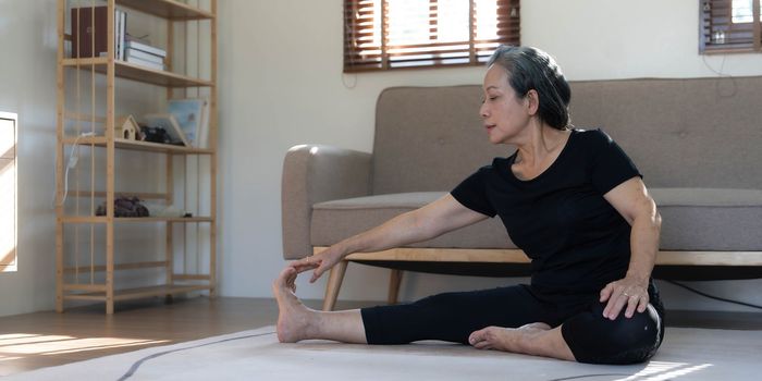 Healthy and happy 60s retired Asian woman in workout clothes practicing yoga in her living room.