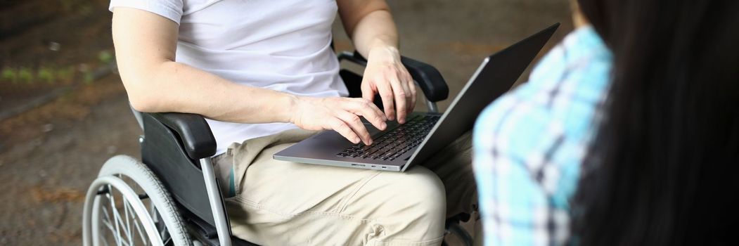 Man in wheelchair and woman work remotely while sitting in park