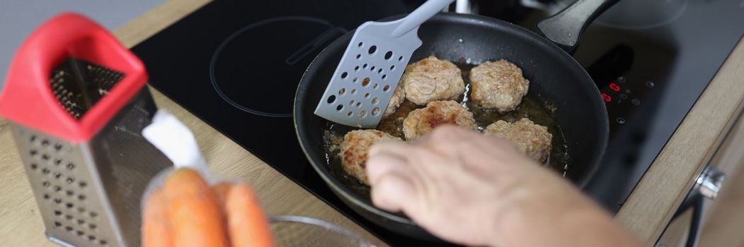 Fried cutlet in the hands of a cook against the background of a frying pan and an electric stove