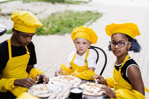 Childhood cook activity of multinational children of black african and caucasian kids. Happy company of multiethnic children cooking dough.