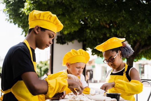 Happy company of multiethnic children cooking dough. Childhood cook activity of multinational children of black african and caucasian kids.