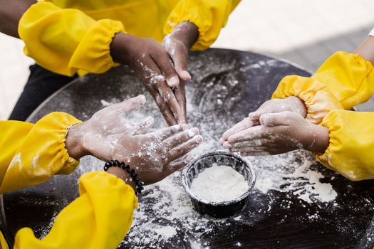 Hands of multinational children cooks play with flour for dough and having fun close-up. Young cooks children cooking khachapuri