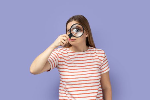 Funny positive woman standing, holding magnifying glass and looking at camera with big zoom eye.
