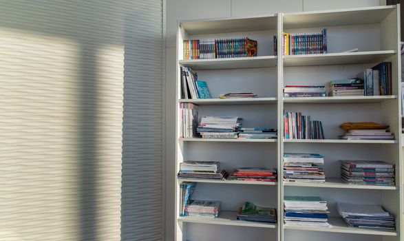 Library of shared facility at living room of home condominium. Different books are arranged on a white bookshelf.