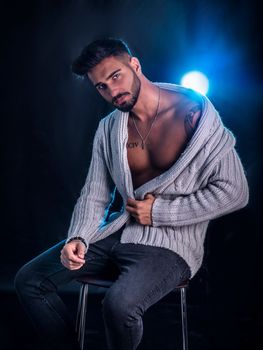 Attractive young man sitting on stool, wearing wool sweater