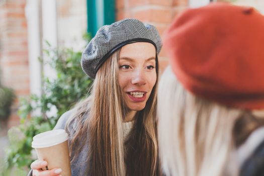Portrait young female best friends talking to each other discussing interesting themes during free time hipster girls joking and having fun together enjoying recreation with coffee to go on urban background