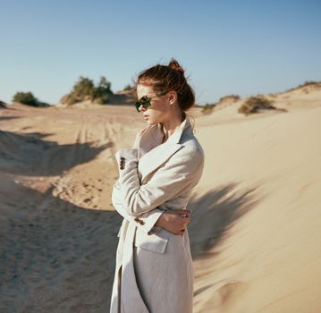 fashionable woman in a light jacket and sunglasses posing against the backdrop of the desert
