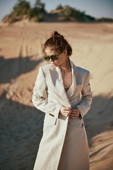 fashionable woman in a light jacket and sunglasses posing against the backdrop of the desert