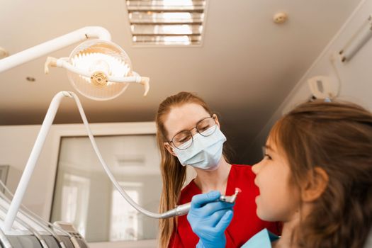Child dentist makes professional teeth cleaning close-up in dentistry. Professional hygiene for teeth of child in dentistry. Pediatric dentist examines and consults kid patient in dentistry