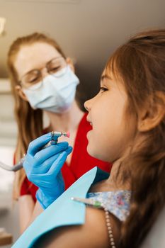 Professional teeth cleaning for child girl in dentistry. Professional hygiene for teeth of child. Pediatric dentist examines and consults kid patient in dentistry.