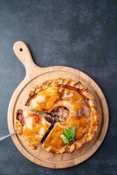 Homemade meat pie with greenery on wooden cutting board on dark table