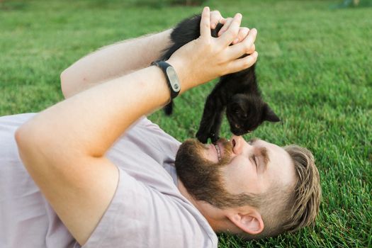 Close-up of Man with little kitten lying and playing on grass - friendship love animals and pet owner concept